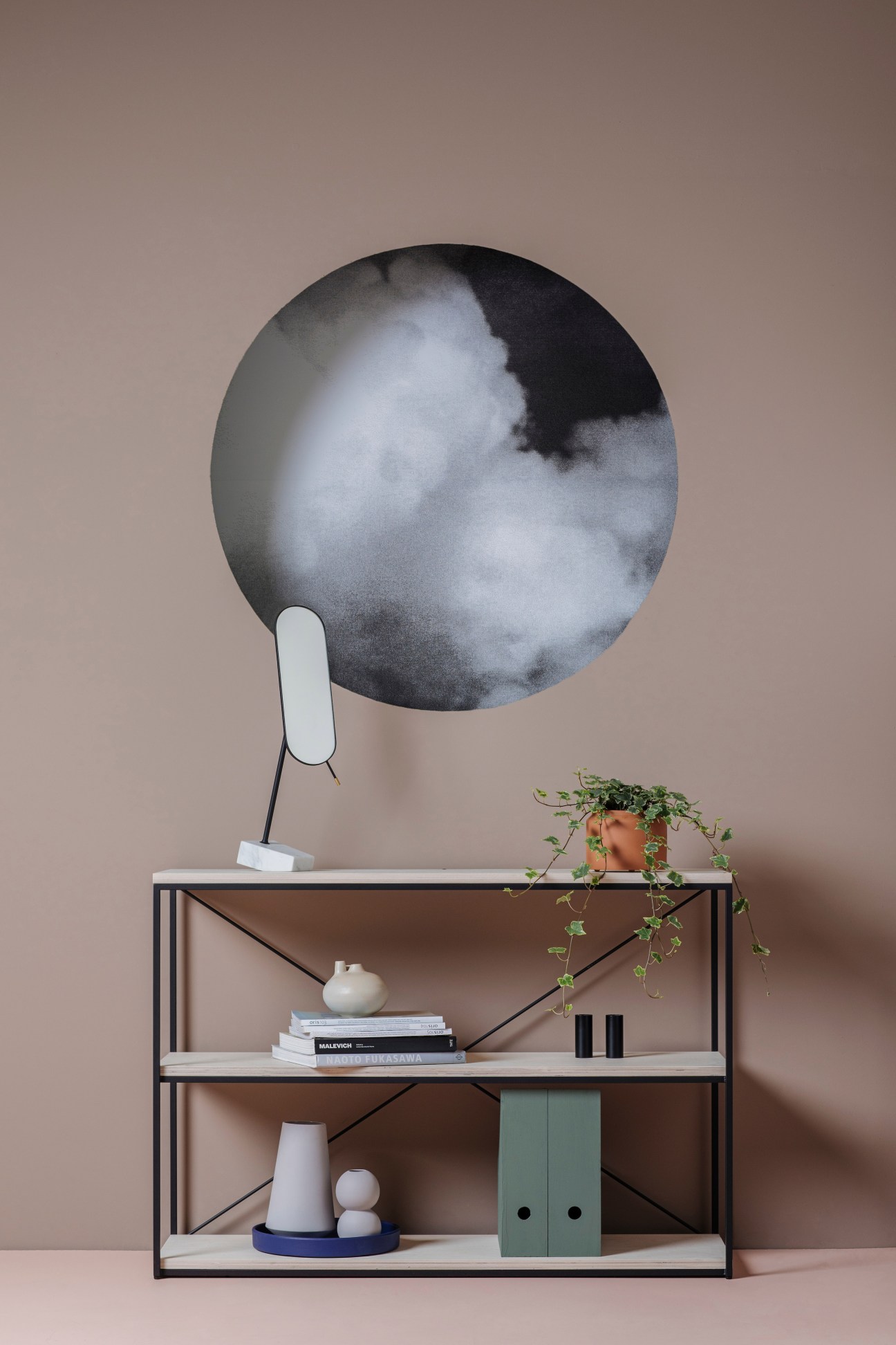 Pendulum mirror with metal frame displayed on shelving unit with decorative objects.