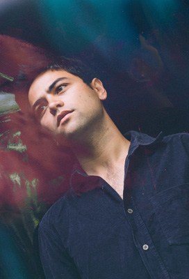 Portrait of a Welsh-Indonesian male musician against a colorful abstract background.