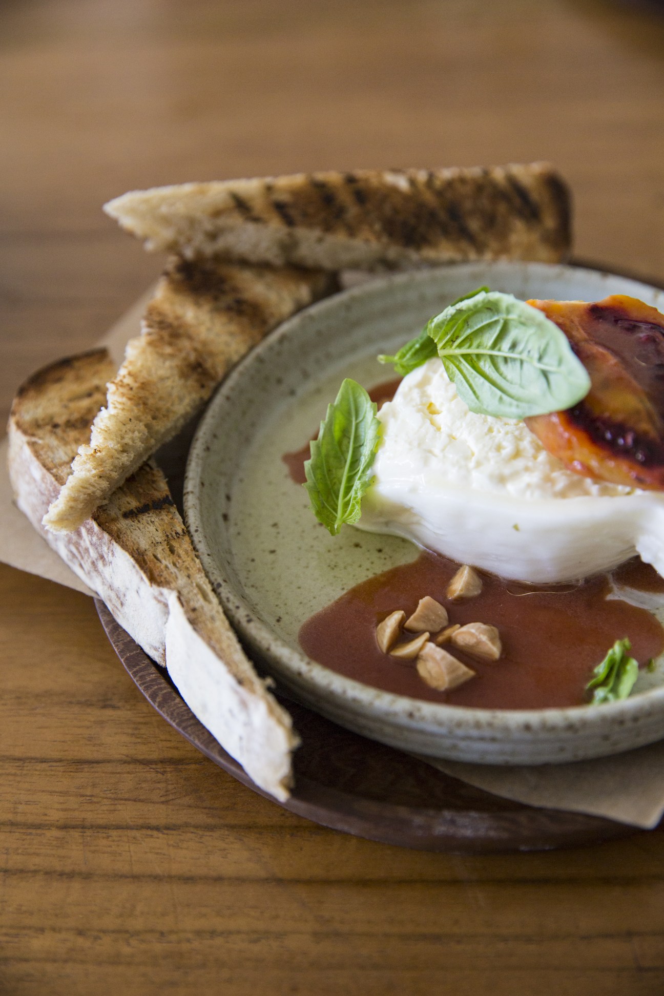 Poached egg with white cheese on toast garnished with basil leaves and nuts on a grey plate.