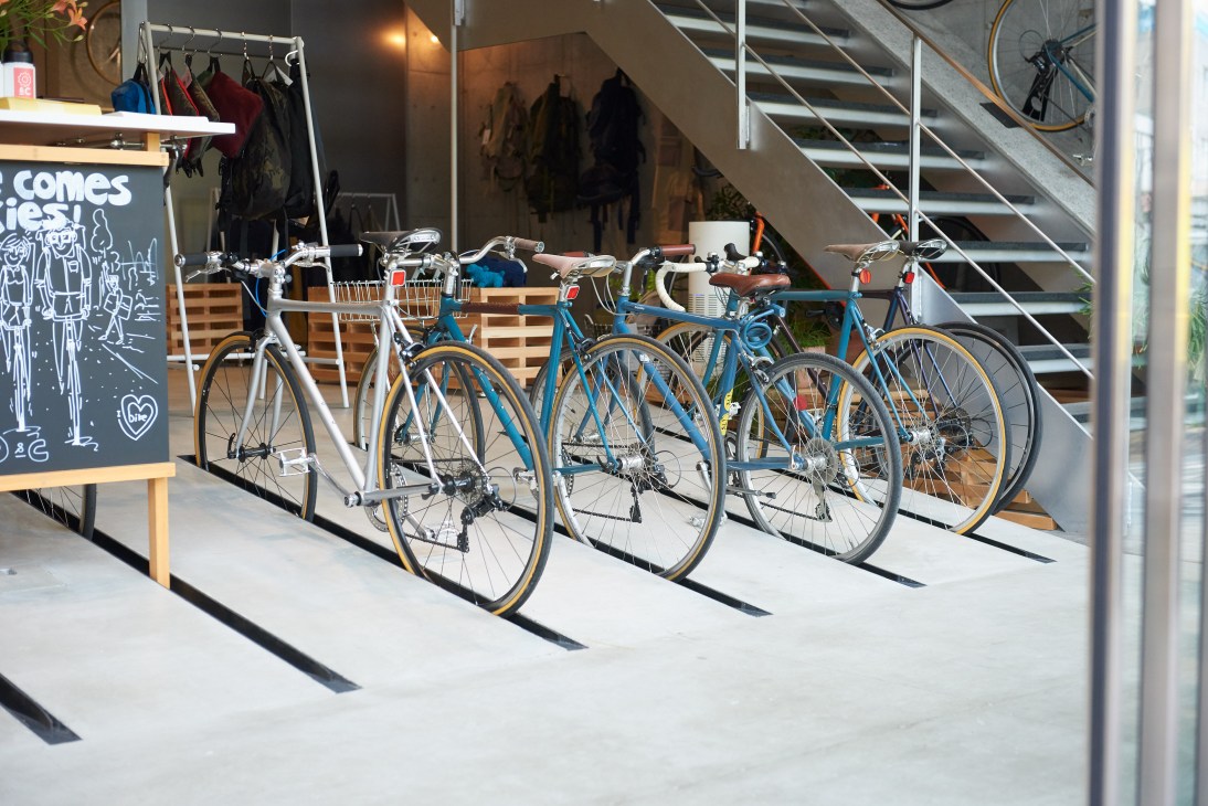 Bicycles parked in front of Ratio & C café in Tokyo, with one silver and three blue bikes displayed near the storefront.