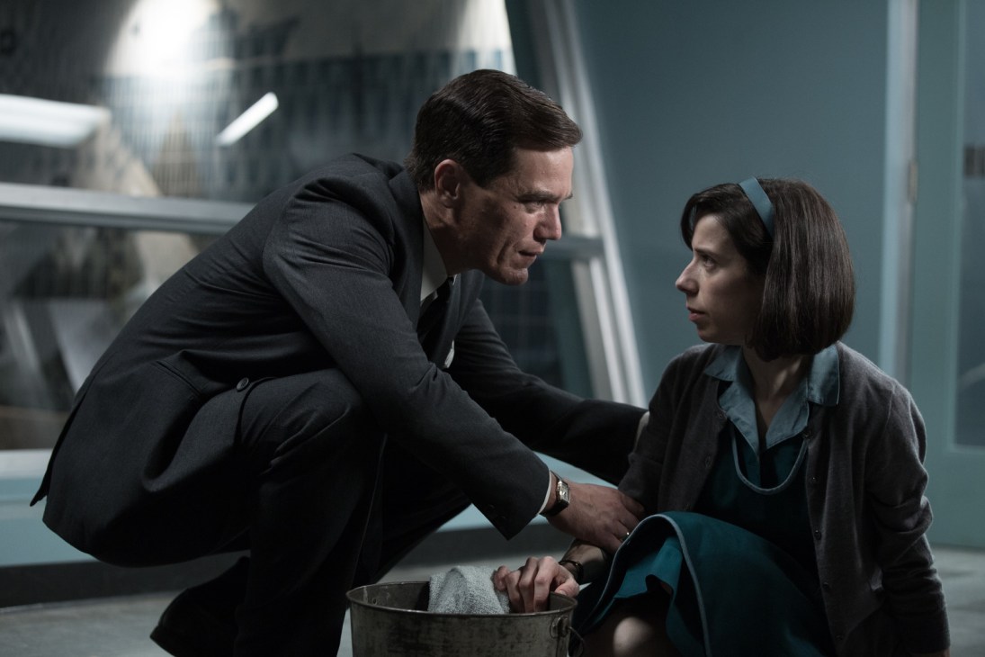 A man in a dark suit crouches beside a woman in a 1950s laboratory setting from The Shape of Water.