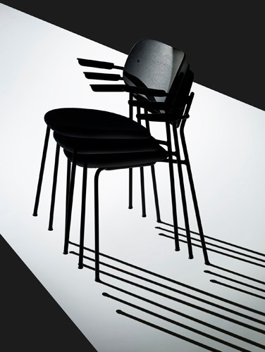 Stacked black chairs with metal legs casting shadows on a diagonal split background.
