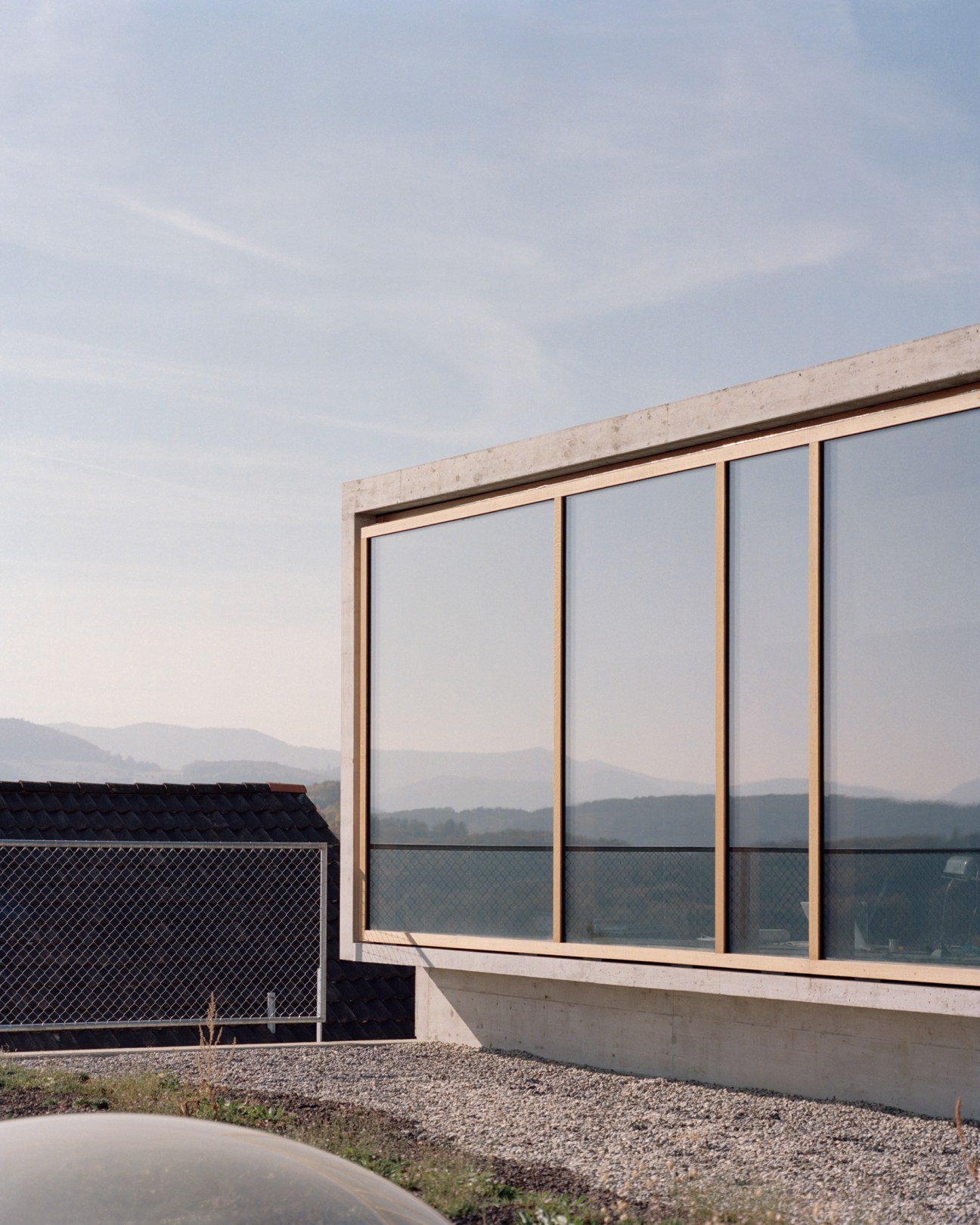 Minimalist workspace with large timber-framed windows overlooking mountains in Nuglar, Switzerland.
