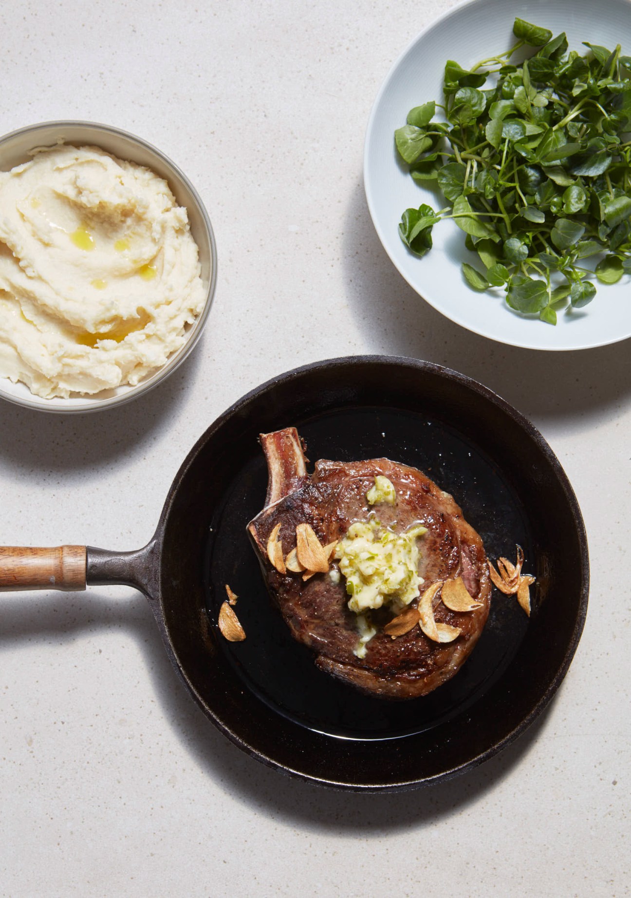 Seared rib-eye steak topped with lime and chilli butter and crispy garlic in a cast iron skillet, served with cauliflower and parmesan mash and watercress.