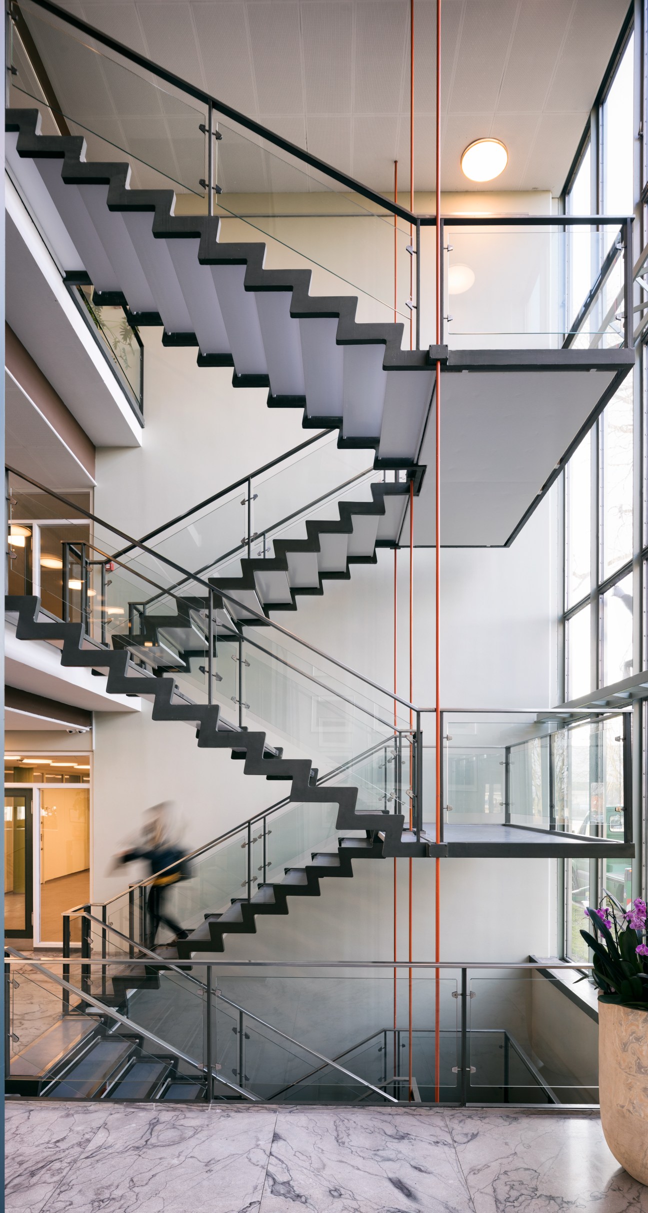 Suspended staircase with thin stainless steel steps and glass balustrades at Rødovre town hall, Denmark.