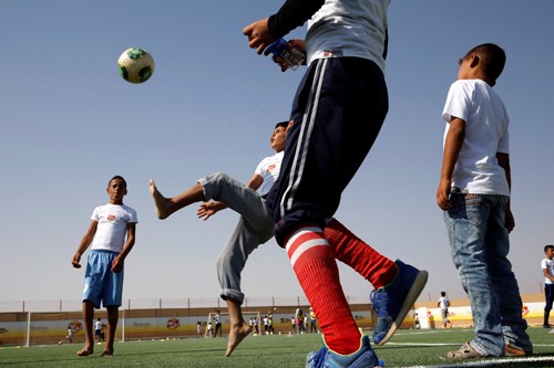 Children playing soccer on a field in Jordan, kicking a ball together.