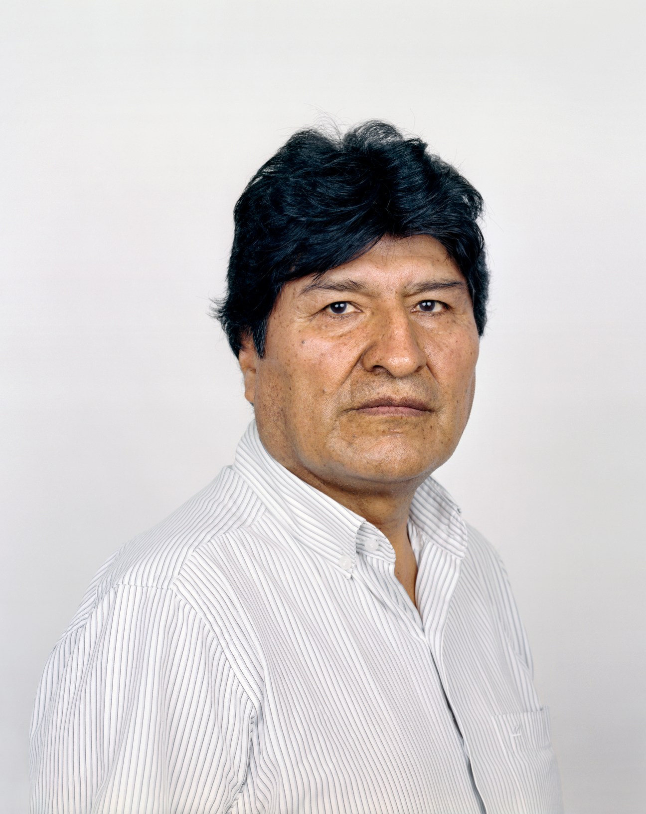 Portrait of Evo Morales wearing a white striped shirt against a plain background