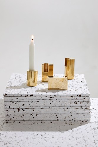 Brass candlesticks with a white candle arranged on a textured white surface.