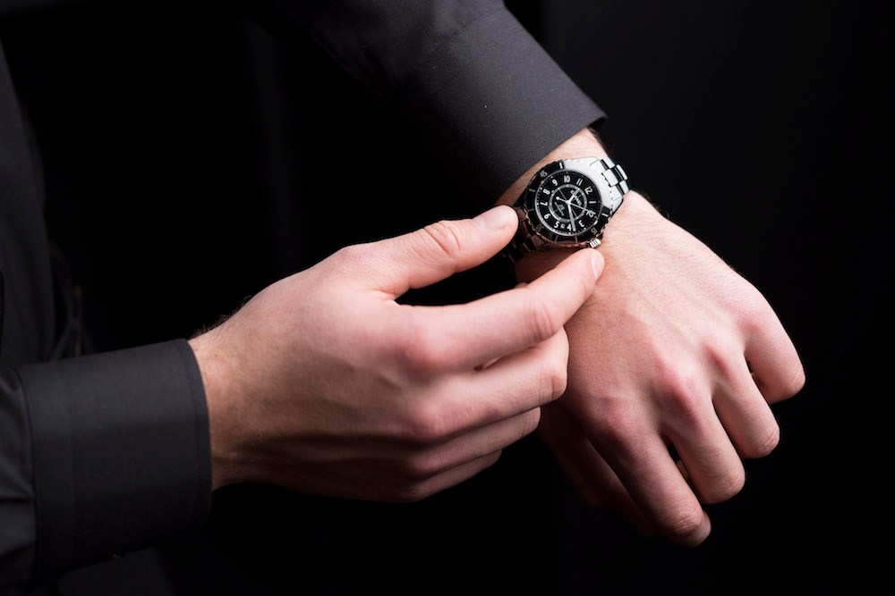 Man in black suit displaying a Chanel J12 watch with refined bezel on his wrist