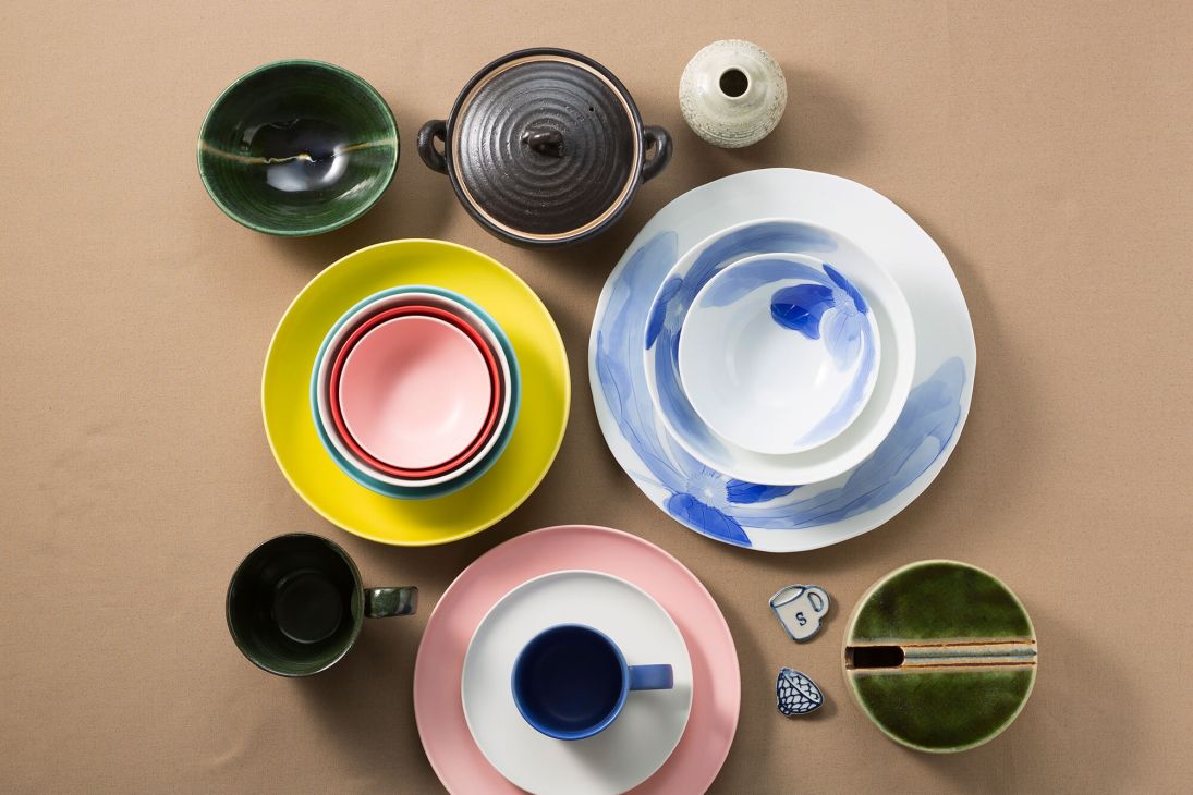 Collection of colorful ceramic bowls, plates, and vessels arranged on a beige surface.