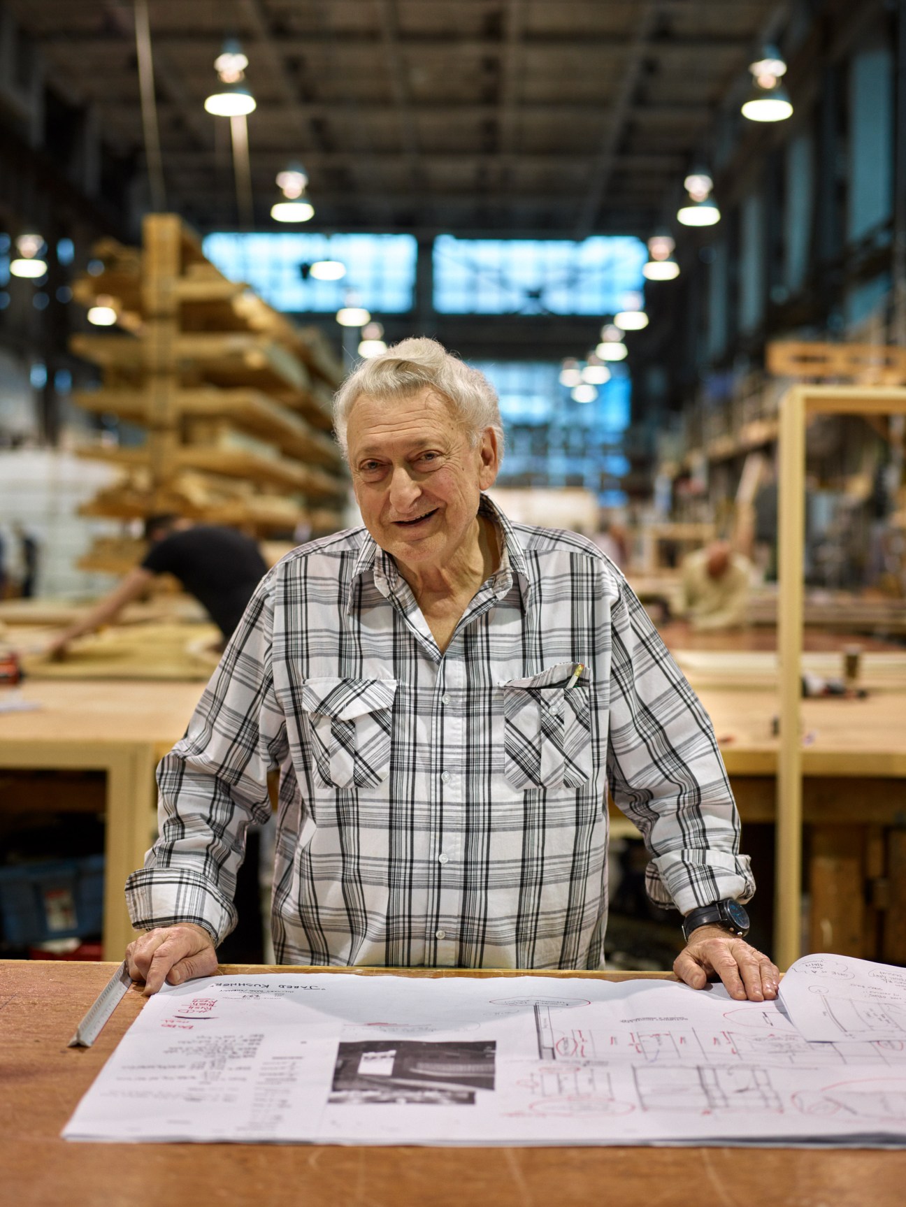 Stephen Demo De Maria, 79-year-old foreman, stands at a workbench with blueprints in a Brooklyn Navy Yard workshop.