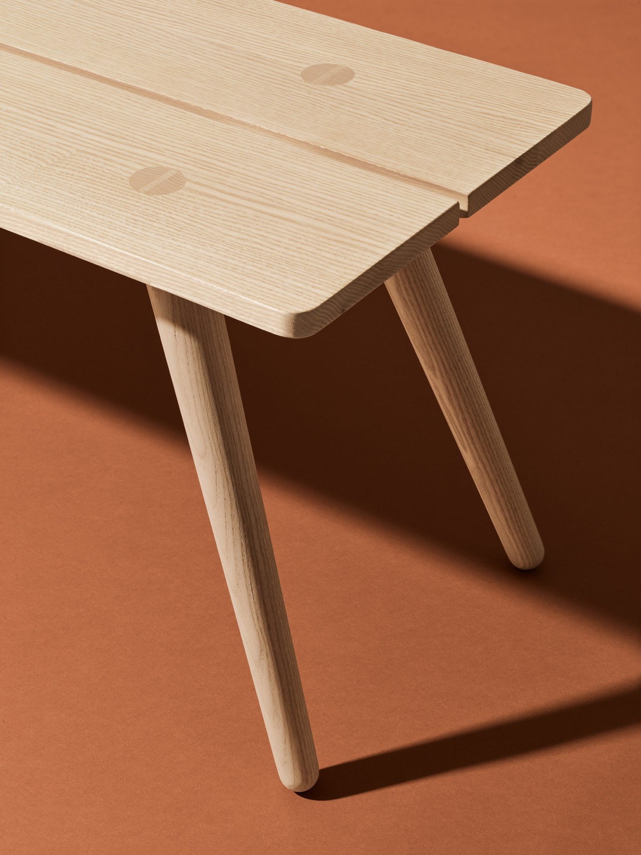 Light wood bench with hand-turned legs and visible wood grain against an orange background.