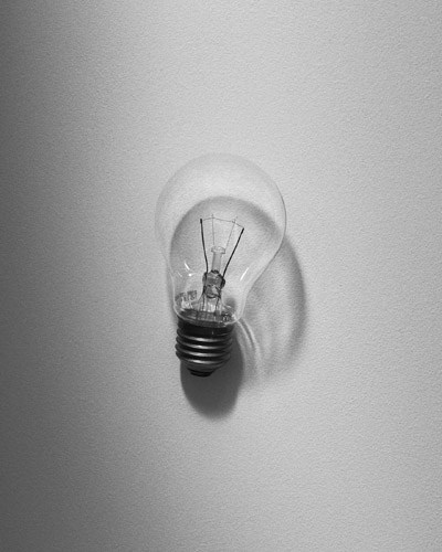 Black and white photograph of an incandescent lightbulb mounted on a white wall.