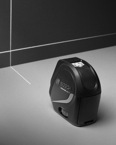 Bosch cross-line laser level projecting guides onto a white wall for precise picture hanging.