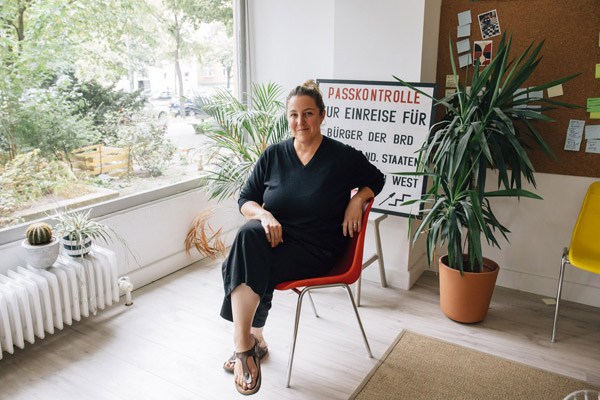 Woman in black outfit sitting on red chair in bright office space with plants and windows.