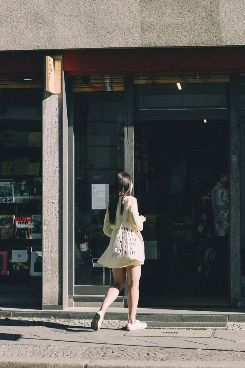Woman entering Do You Read Me?! magazine shop in Berlin carrying a white shopping bag.