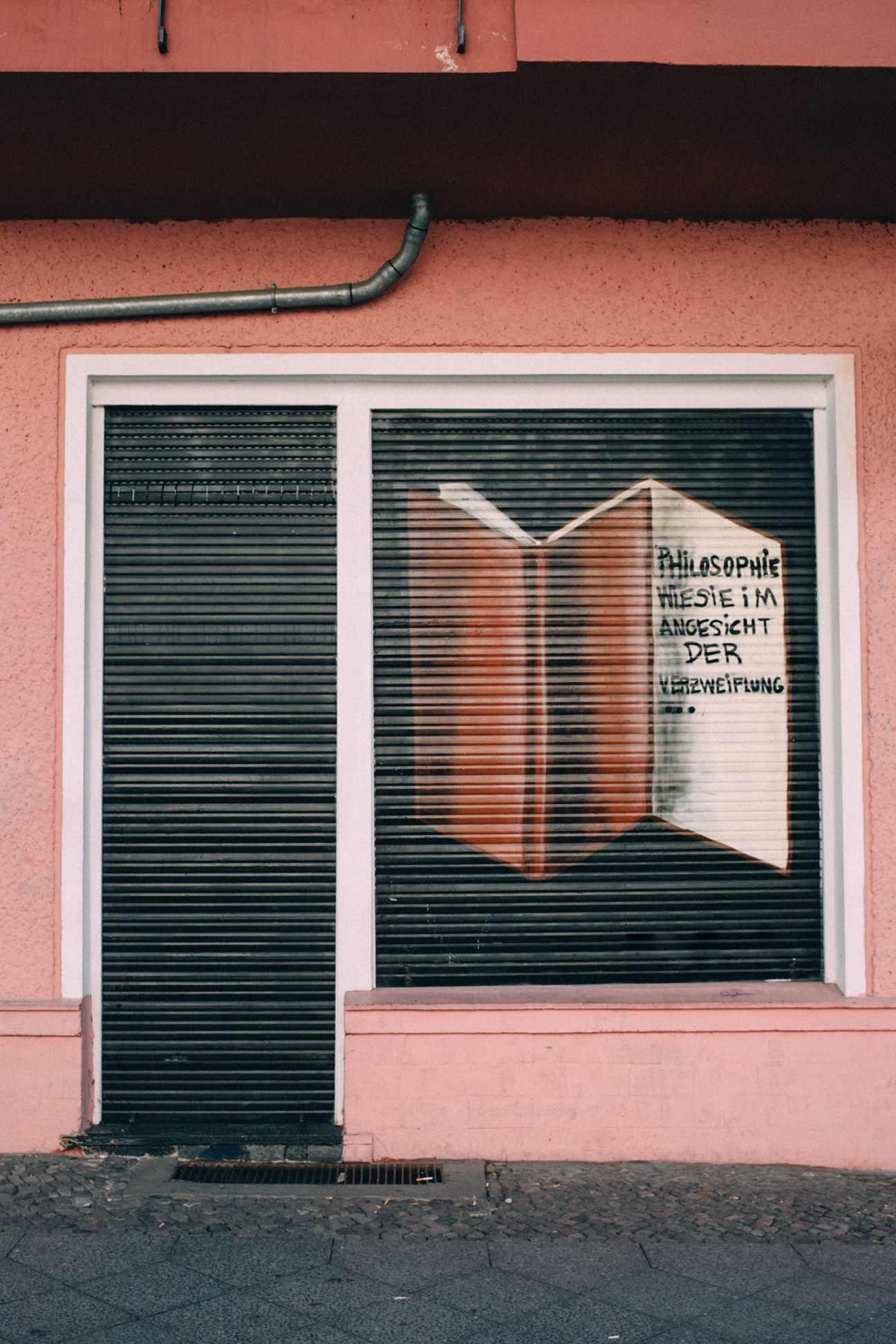 Pink storefront with green shuttered door and window displaying an open book illustration and German text.