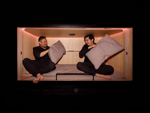 Two founders sit facing each other inside a minimalist sleep pod with wooden walls and warm lighting.