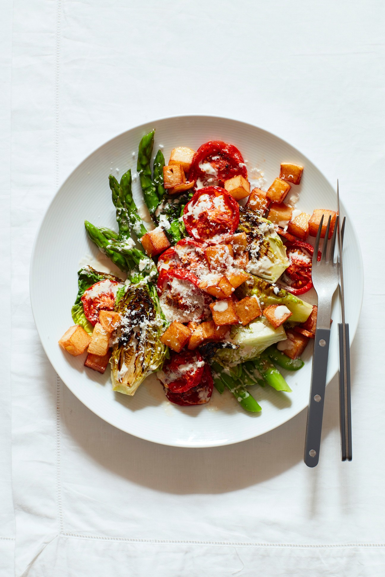 Slow-roasted tomato, potato and grilled asparagus salad with anchovy dressing on a white plate.