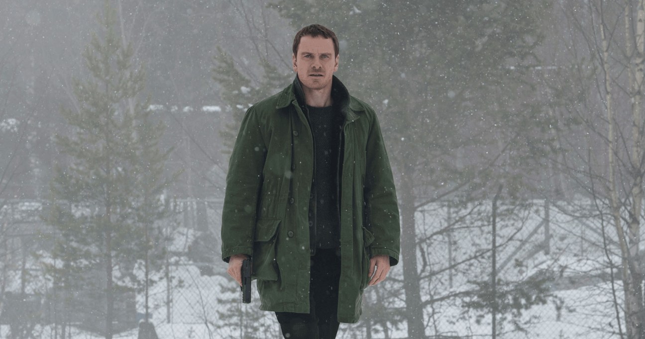Man in green coat standing in snowy forest during heavy snowfall.