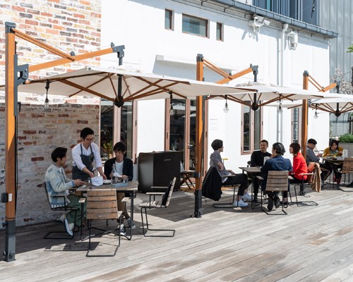 Outdoor wooden deck at Søholm restaurant in Tokyo with diners seated under orange and black umbrellas.