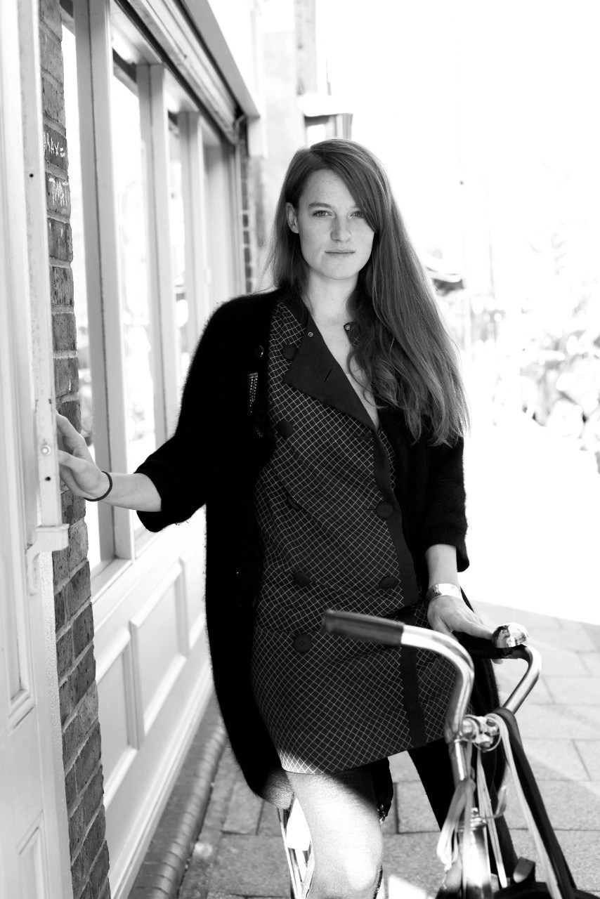Black and white portrait of Sophie Grove standing on a street with a bicycle, wearing a blazer.
