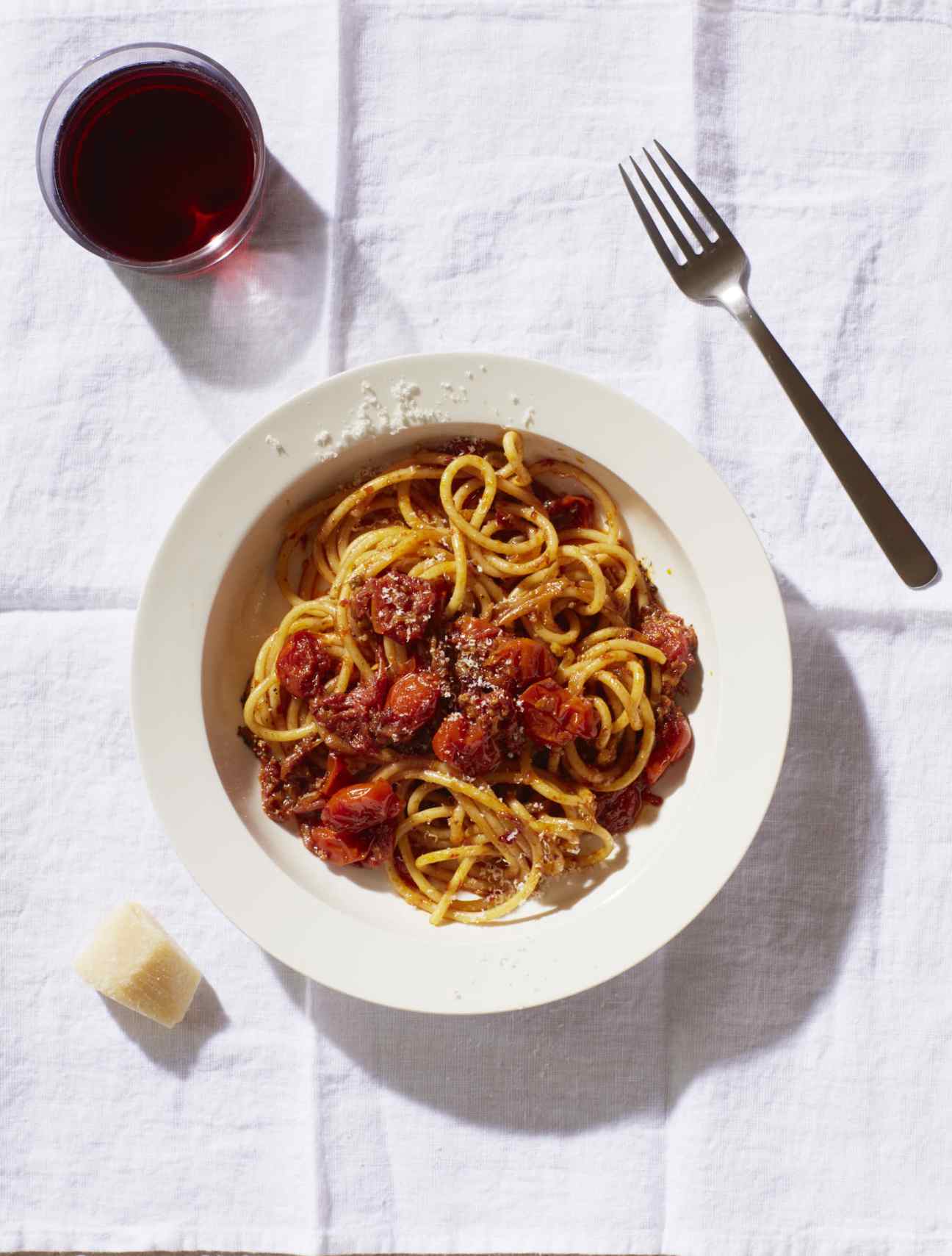 Bowl of nduja, chilli and tomato bucatini pasta with a fork and glass of red wine on white linen.