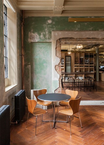 Minimalist workspace with round table, wooden chairs, and exposed green wall in converted factory.