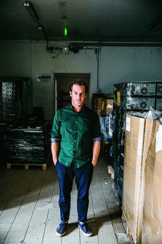 Man standing in warehouse with ice production equipment and packaged ice bags.