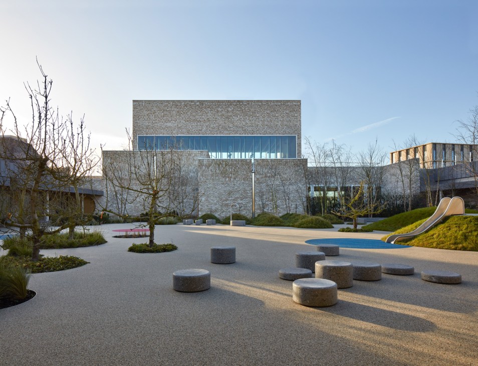 Storey's Field Centre exterior showing modern brick building with blue-framed windows and playground featuring slide and seating areas.