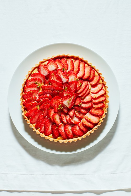 A strawberry tart with sliced red strawberries arranged in a spiral pattern on a custard filling in a pastry shell, served on a white plate.