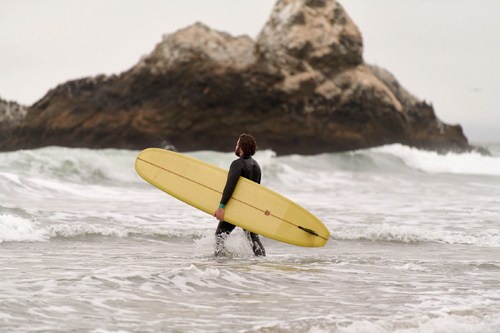 Surfer in black wetsuit carrying yellow surfboard entering the ocean at Ocean Beach, San Francisco.
