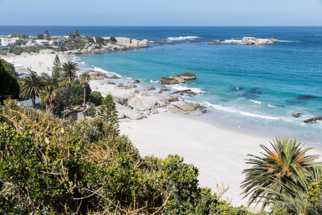 Clifton Beach in Cape Town with white sand, turquoise water, granite boulders, palm trees and whitewashed houses on the coastline.
