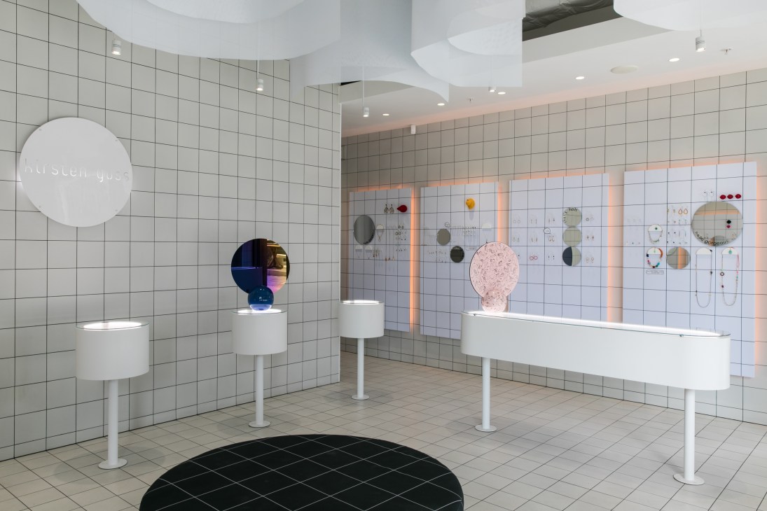 Kirsten Goss jewelry store interior with white tiled walls, display pedestals, and illuminated jewelry pieces.