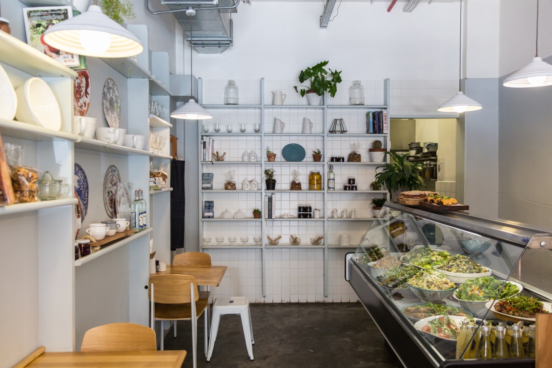 The General Store restaurant interior with white shelving, pendant lights, wooden chairs and a refrigerated display counter with salads.