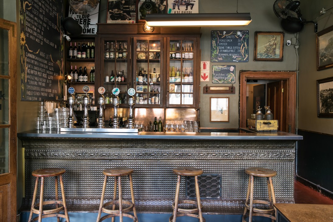 The Power and the Glory bar interior with wooden stools, beer taps, and shelved bottles behind the counter.