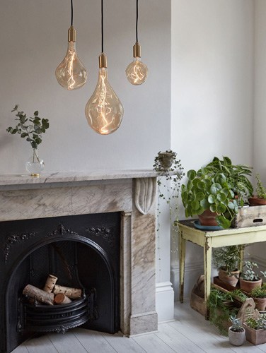 Three pendant lights with amber glass bulbs hanging above a fireplace mantelpiece with potted plants.