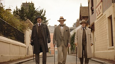 Three men in period clothing walking down a street in The Happy Prince film.