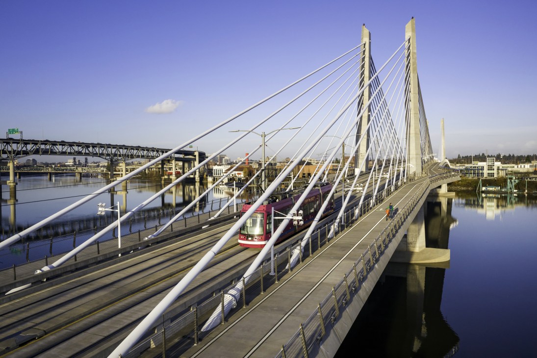 Tilikum Crossing cable-stay bridge spanning the Willamette River with a red tram crossing and pedestrian walkways.