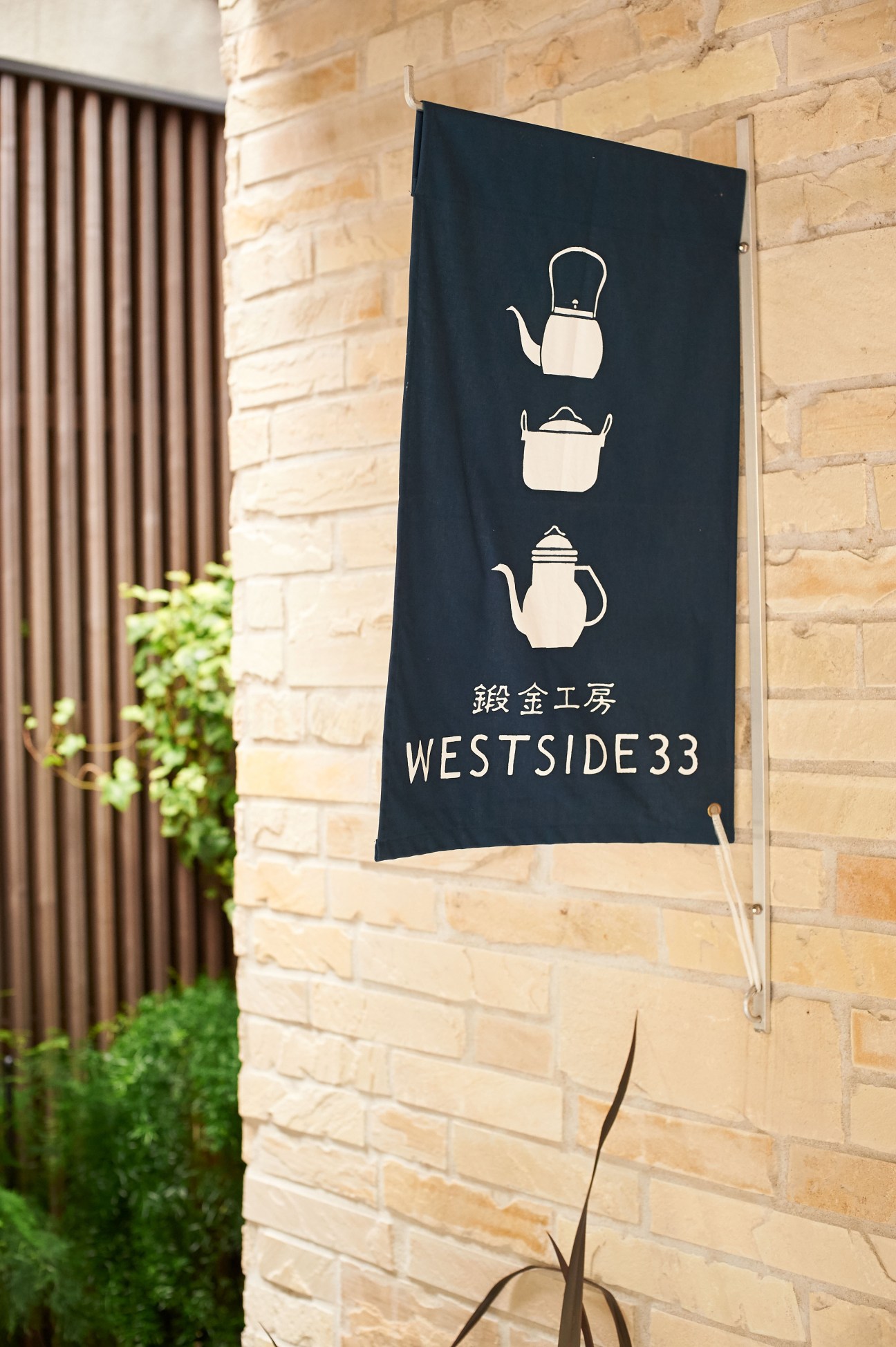 Westside33 shop sign with teapot and cooking pot illustrations on black banner mounted on brick wall.