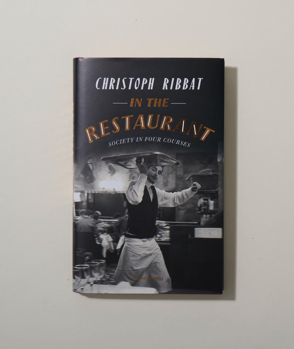 Book cover of 'In The Restaurant' by Christoph Ribbat, featuring a black and white photograph of a chef in a kitchen.