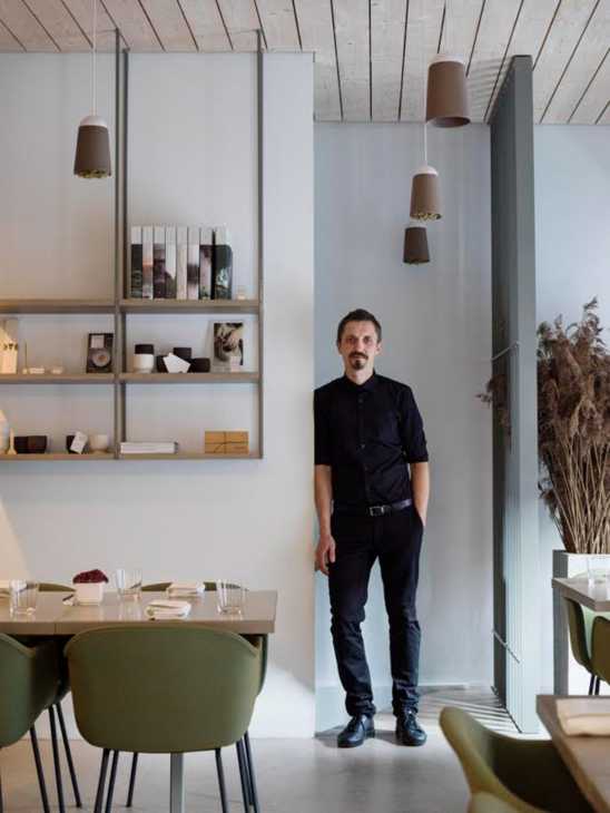 Man in black shirt standing in modern restaurant interior with pendant lights and shelving.