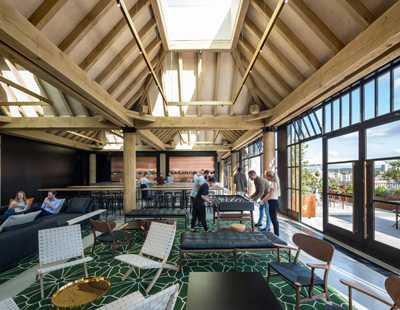 Interior of a rooftop restaurant space with exposed wooden beams, skylights, and modern seating areas overlooking a city.