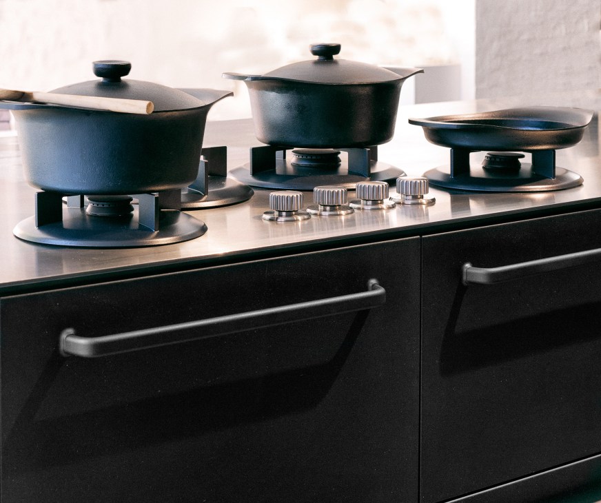 Vipp kitchen stovetop with dark cookware and metal knobs on black cabinetry.