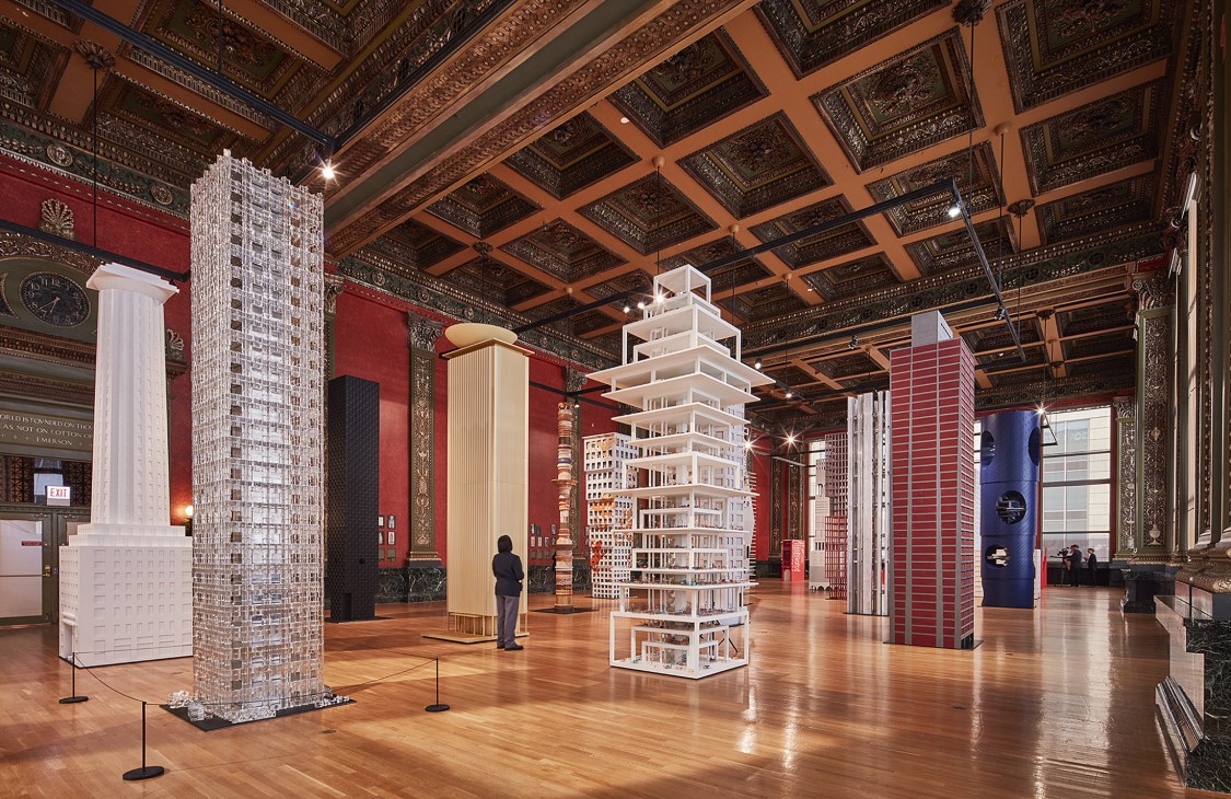 Interior view of Chicago Architecture Biennial exhibition with architectural models and installations displayed in ornate historic hall.