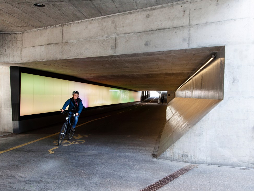 Cyclist riding through a well-lit underground tunnel with wooden ceiling and illuminated wall panels at Winterthur train station.