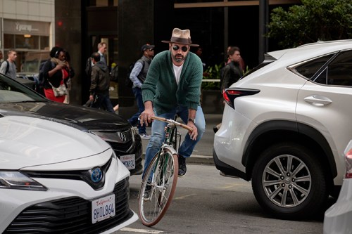 Man in cycling gear riding a bicycle between parked cars on an urban street.