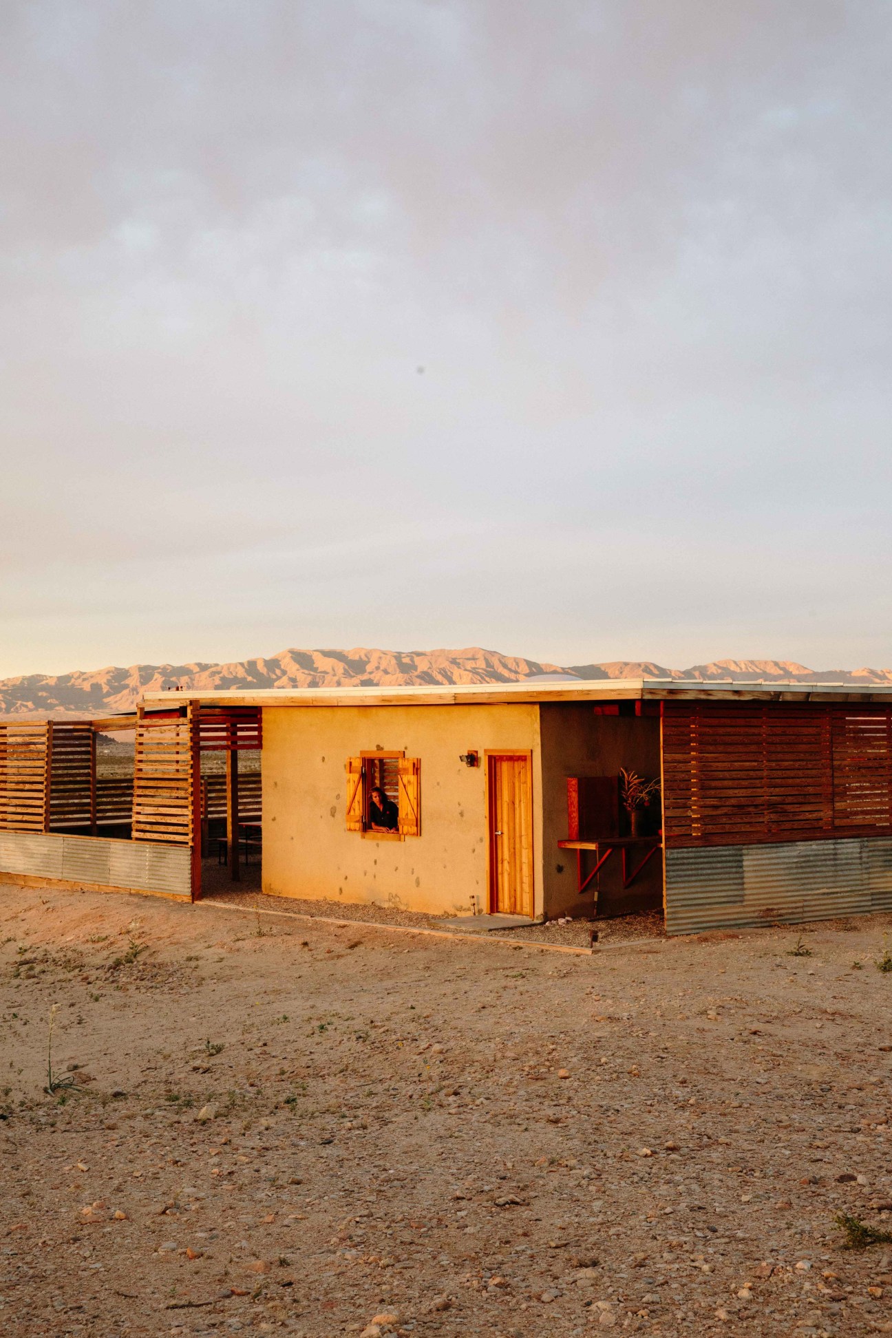 A colorful single-story building with yellow and orange walls and wooden louvered panels in a desert landscape.
