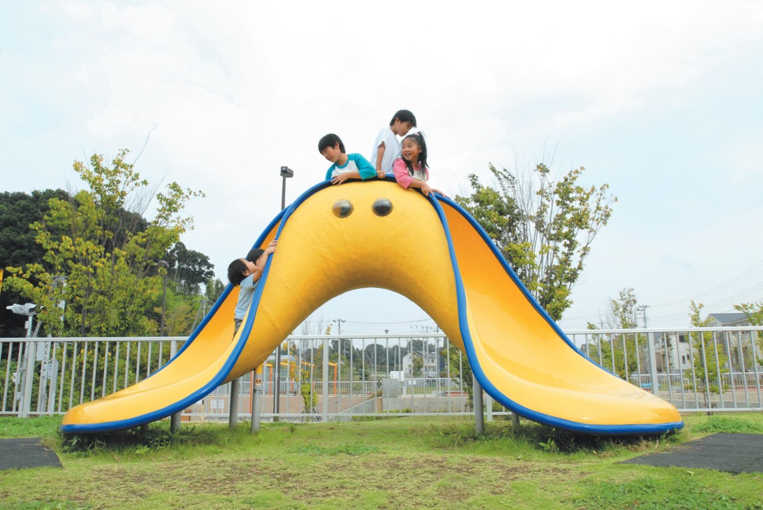 Children playing on a yellow slide with blue railings at Minezuka Park in Habikino, Japan.