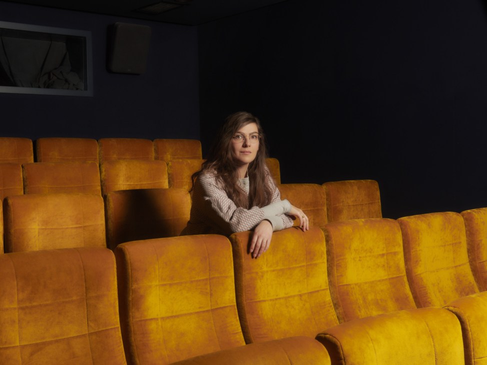 Woman seated alone among yellow-orange cinema seats in a screening room.